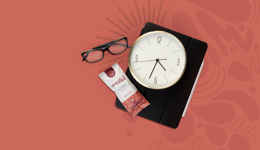 Omega 3 cranberry granola bar with a iPad, digital pen, pair of black frame glasses and a clock